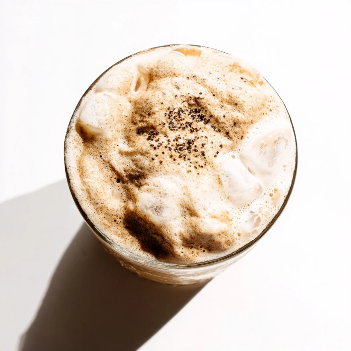 Creamy whipped Dalgona coffee floats like a cloud over cold milk in a glass filled with ice cubes.