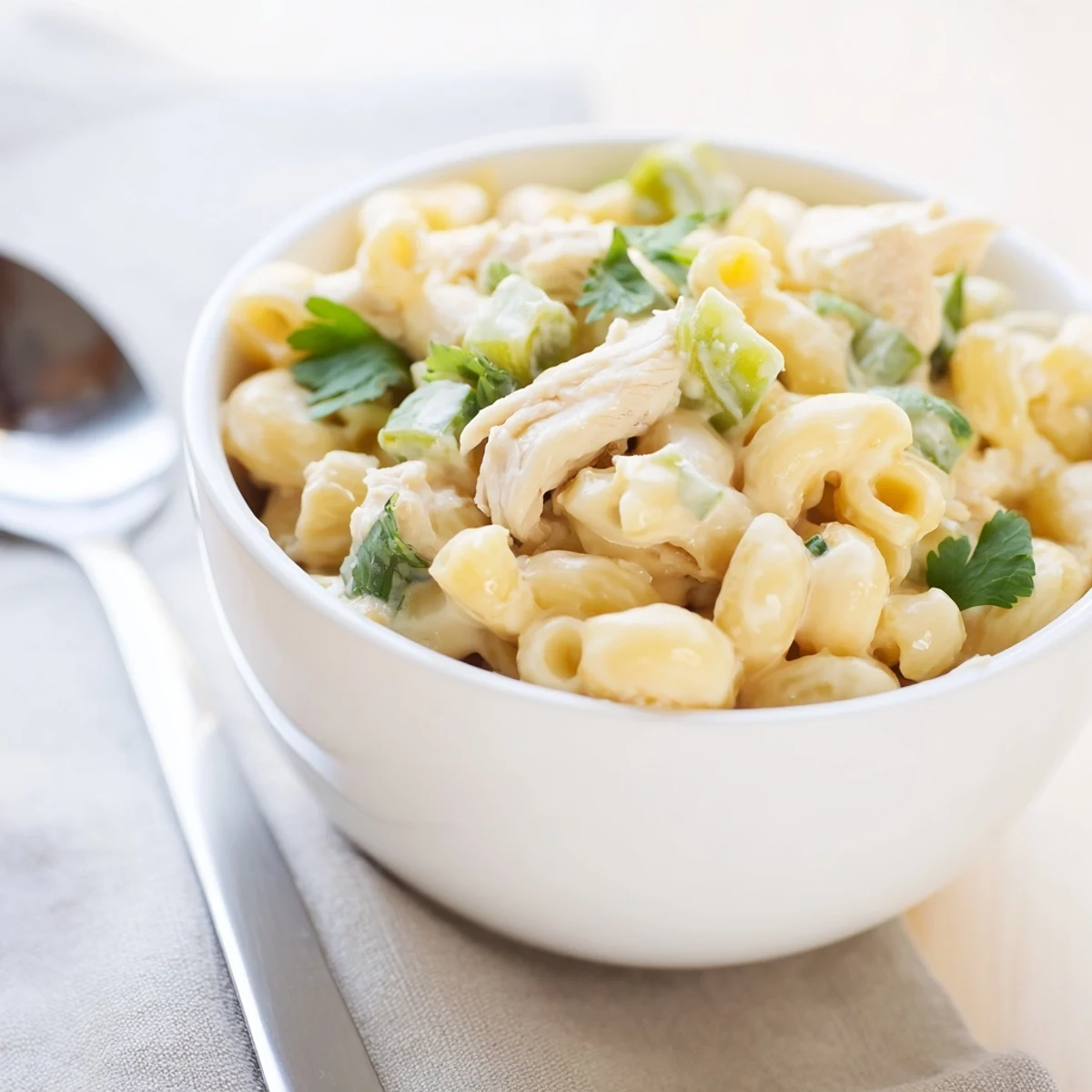 A close-up of creamy Green Chili Chicken Mac in a skillet, with tender chicken pieces and melted cheese strings visible.