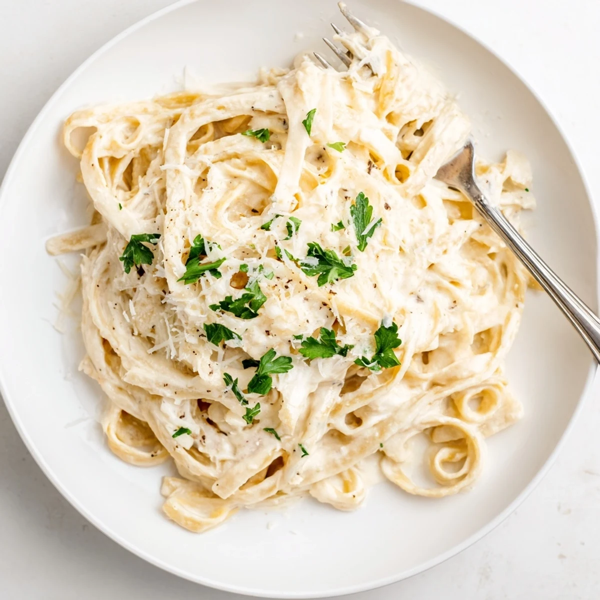 Plated Easy Creamy Cauliflower Alfredo garnished with Parmesan and parsley, featuring tender fettuccine noodles coated in the creamy, low-fat cauliflower sauce.