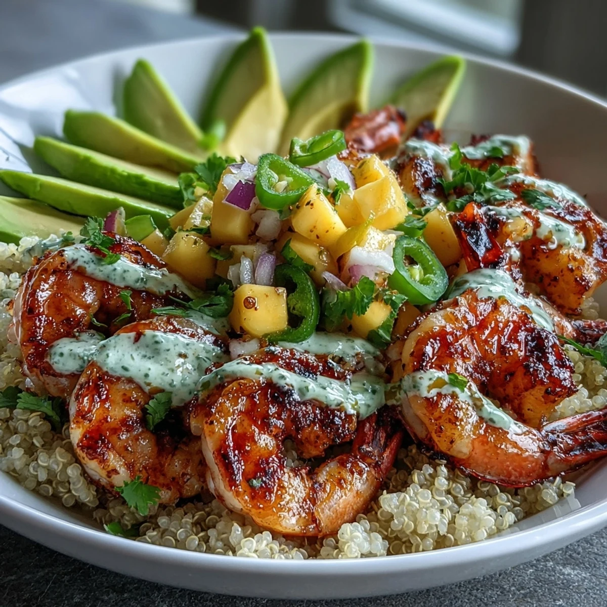 Healthy dinner bowl featuring seasoned grilled shrimp, nutty quinoa, ripe avocado, and fresh mango salsa with a lime chili sauce garnish.