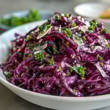 A large bowl of Red Cabbage Coleslaw With Apple and Parmesan, tossed in apple cider vinaigrette and garnished with fresh parsley for a vibrant dinner side.