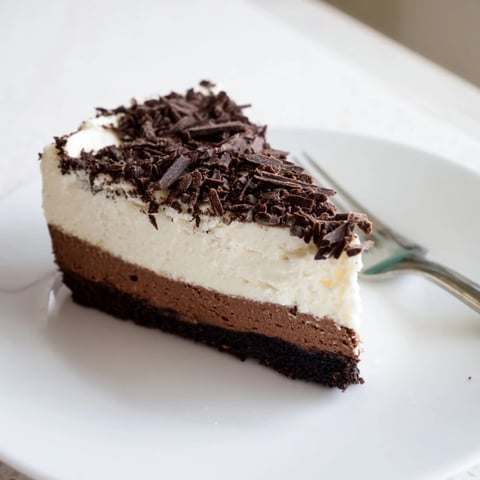 A smooth slice of Lighter Chocolate Cottage Cheese Cheesecake on a white plate, featuring a rich, dark cocoa filling and a crumbly graham cracker crust, ready to be served with fresh berries.