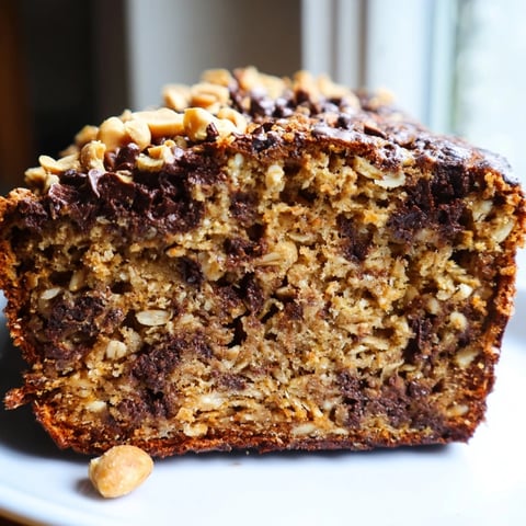 A freshly baked loaf of Chocolate Chip Peanut Butter Oatmeal Banana Bread, sliced thick to reveal moist crumb, melty chocolate chips, and peanut chunks.