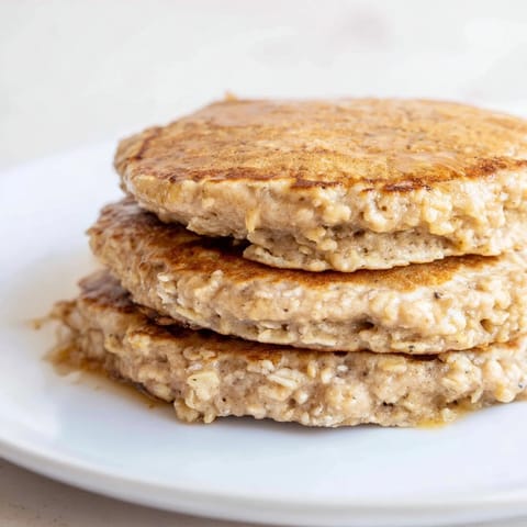 Warm, fluffy Banana Oat Pancakes, ready to be drizzled with maple syrup for a weekend treat.