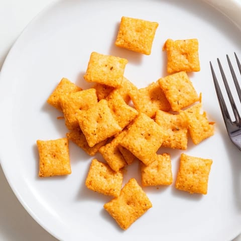 Freshly baked Crispy Cheeto Cheese Crackers on a wooden board, their sharp cheddar and paprika aroma inviting.  