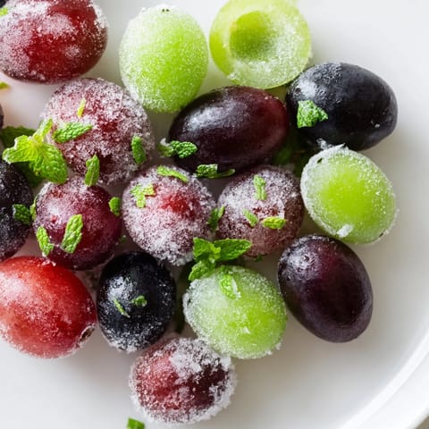 A close-up view of red and green frozen grapes, glistening with frost, ready for a cooling snack.