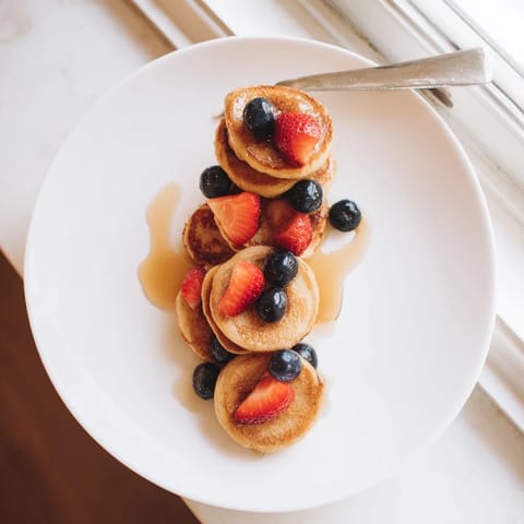 Two small Banana Pancakes cooking on a non-stick skillet, showing bubbles forming on the soft, gluten-free batter.