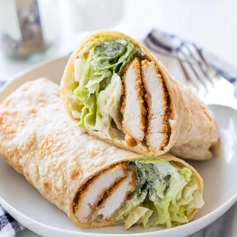 Warm flour tortilla cradles crunchy fried chicken, crisp romaine, and shaved Parmesan, drizzled with creamy Caesar dressing for a delicious lunch wrap.