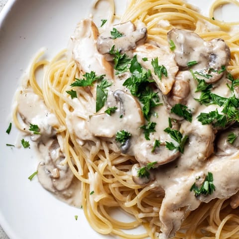 Freshly plated Creamy Mushroom Chicken Spaghettini garnished with parsley, featuring tender chicken and savory mushrooms in a light cream sauce.