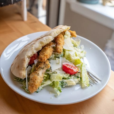 A close-up of crispy herbed chicken Caesar pitas, showcasing fresh romaine, creamy dressing, and lemon wedges.