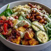 Freshly roasted sweet potato, bell pepper, and zucchini top a warm bowl of Black-Eyed Pea Buddha Bowl, drizzled with creamy tahini dressing.